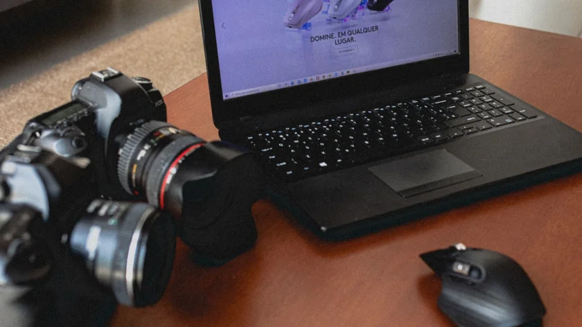 Appareil photo reflex posé devant un ordinateur portable et une souris sur une table en bois.