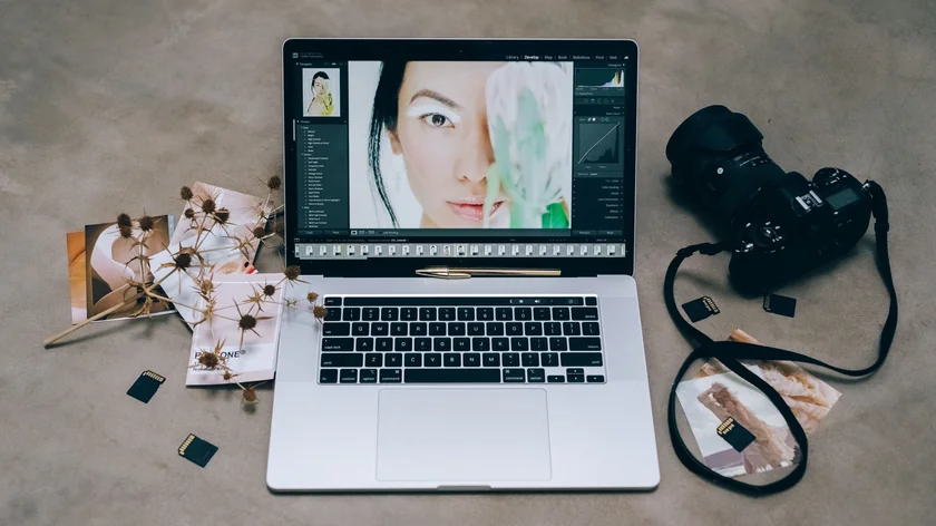 Un appareil photo et des cartes mémoire sont posés à côté d'un ordinateur affichant une photo en retouche.