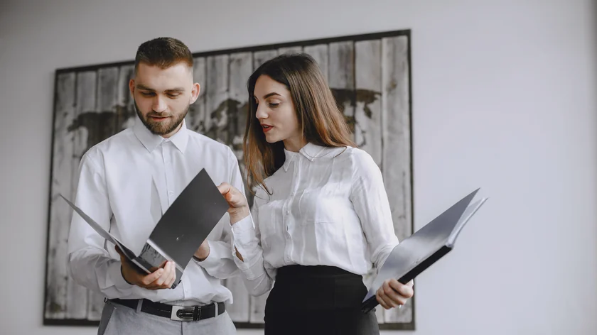 Deux personnes en chemise blanche examinent ensemble des dossiers ouverts dans un bureau.