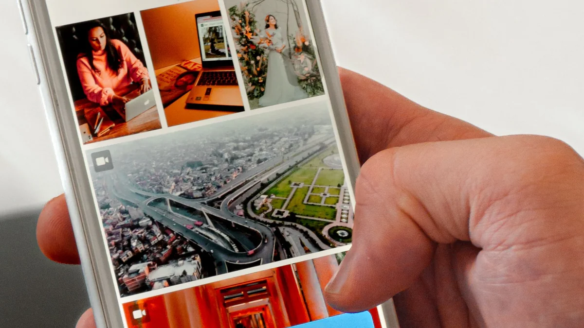 Une main tient un smartphone affichant une grille de photos colorées.
