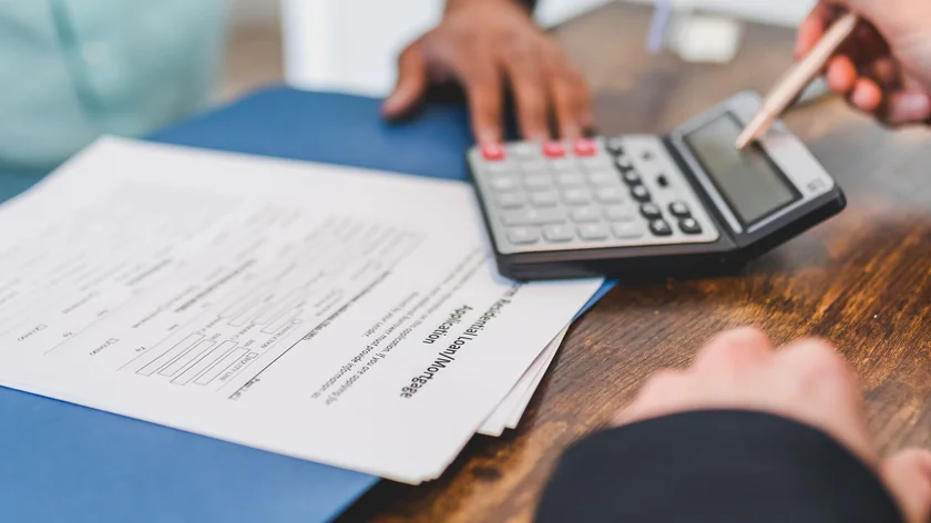 Des mains examinent des documents et utilisent une calculatrice pendant un échange commercial.