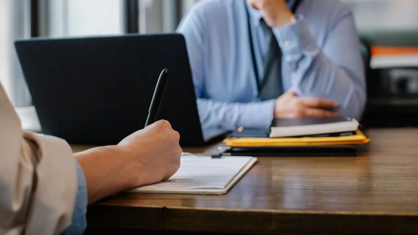 Une personne remplit un formulaire sur papier à côté d’un ordinateur portable.