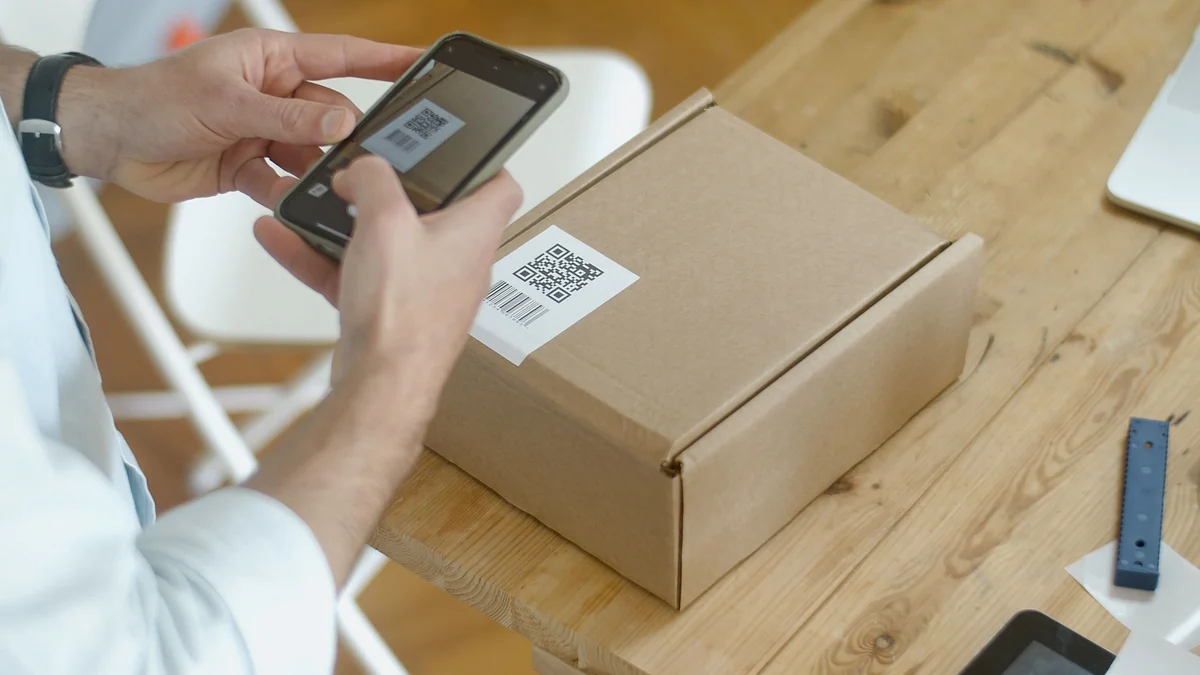Des mains orientent un smartphone vers une étiquette avec un QR code collée sur un carton.