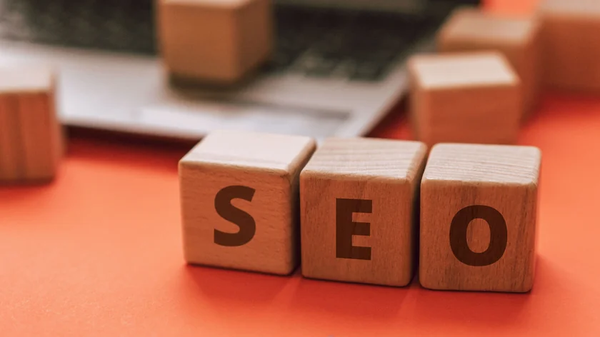 Trois blocs de bois portant les lettres SEO sont posés sur un fond orange.