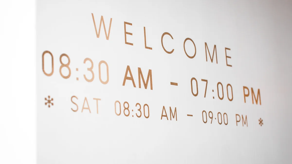 Panneau d’accueil blanc portant le mot « Welcome » et des horaires d’ouverture en lettres dorées.