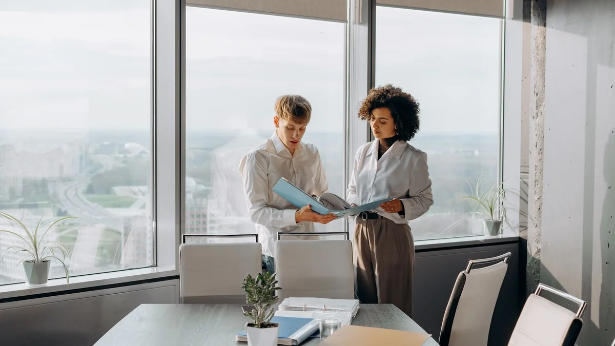 Deux personnes debout dans un bureau lumineux consultant des documents ensemble.