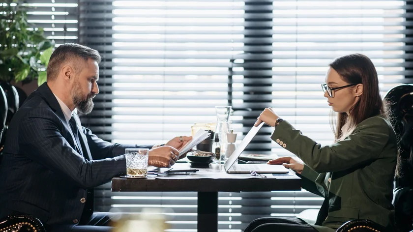 Un homme et une femme consultent des documents et un ordinateur autour d’une table.